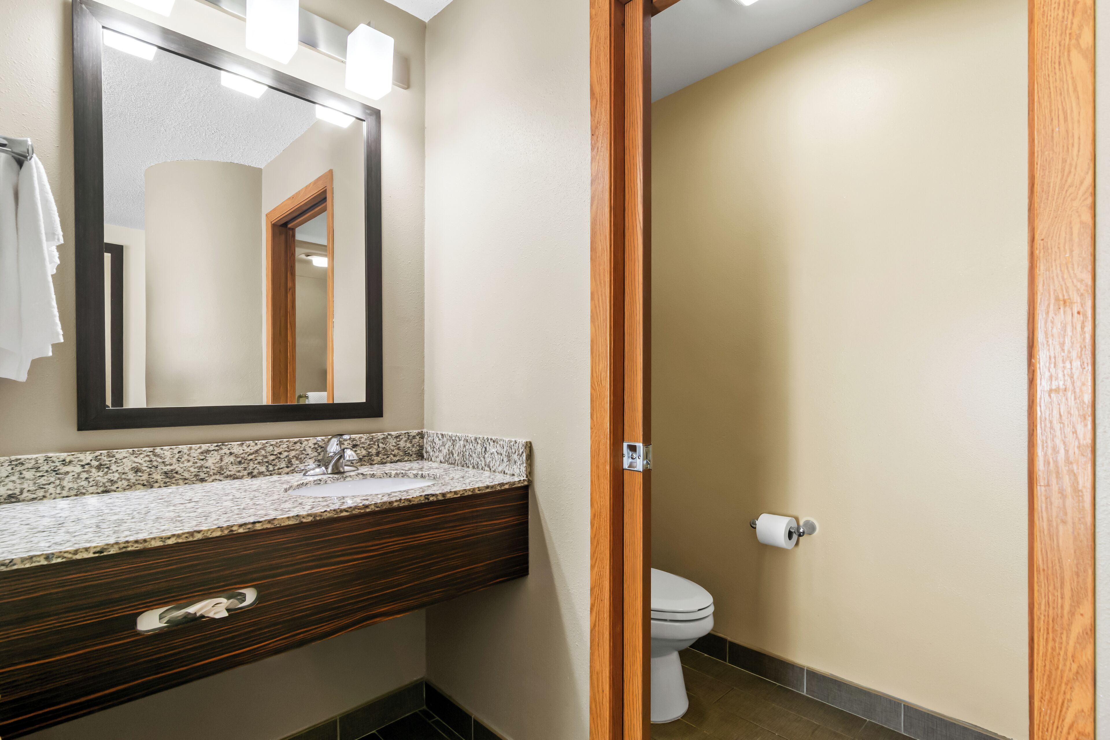 Un baño con lavamanos de encimera de granito, tocador de madera, espejo y retrete.