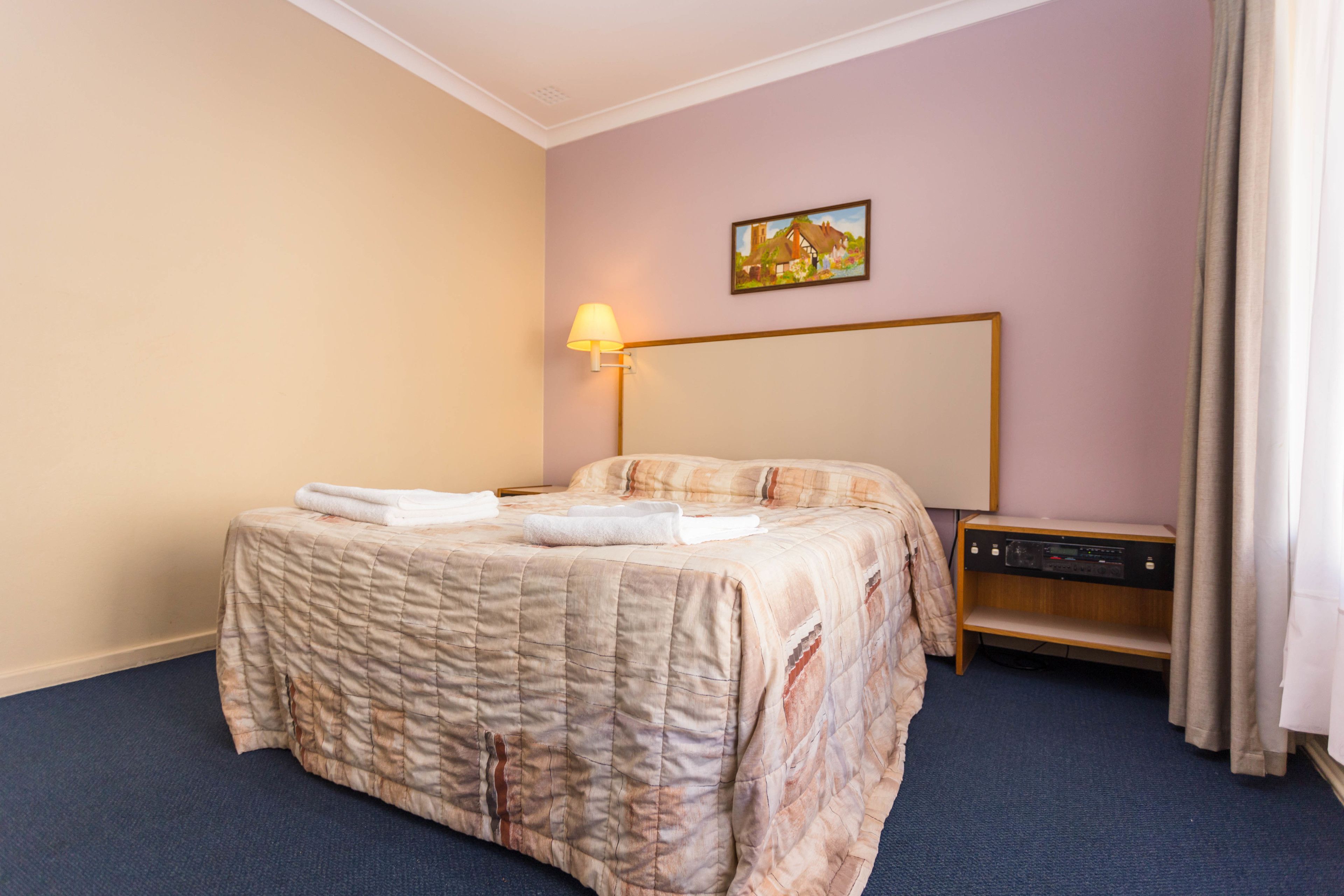 Una habitación de hotel con una cama, una mesita de noche, una lámpara y un cuadro en la pared.
