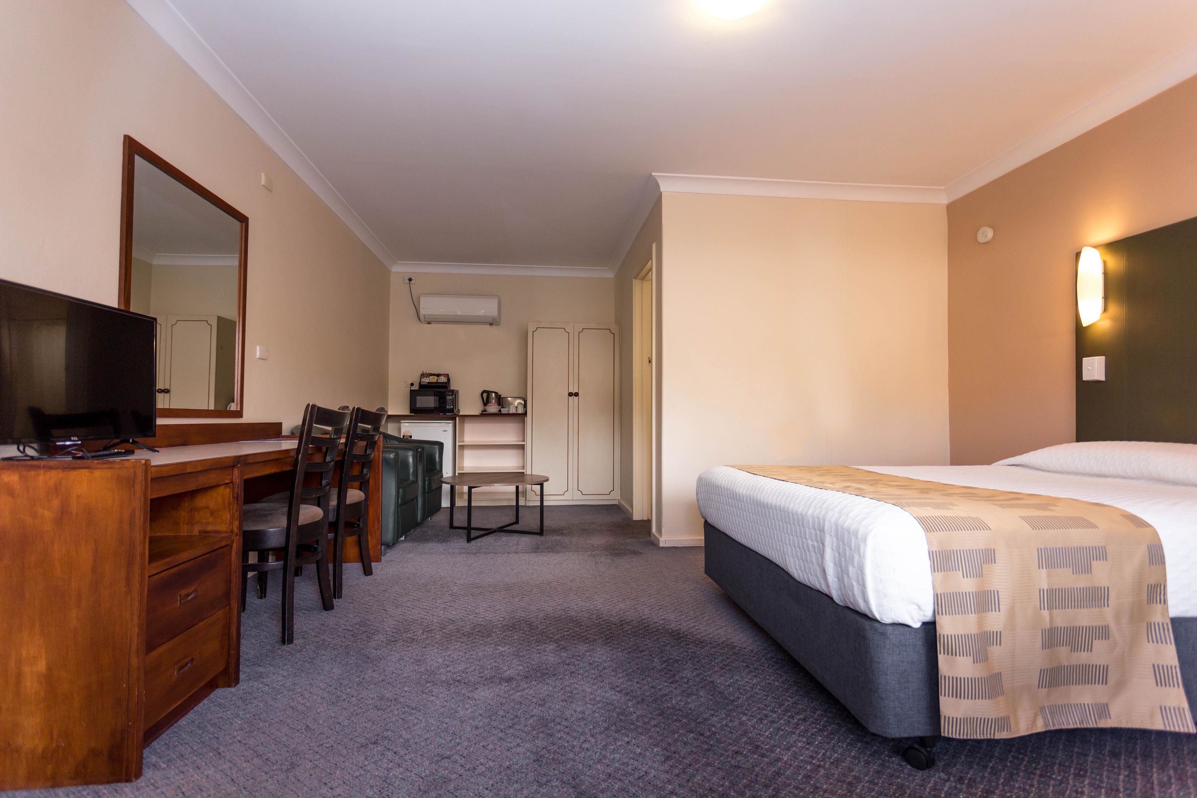 A hotel room with a bed, a desk with a chair, a television, a wardrobe, and a small table.