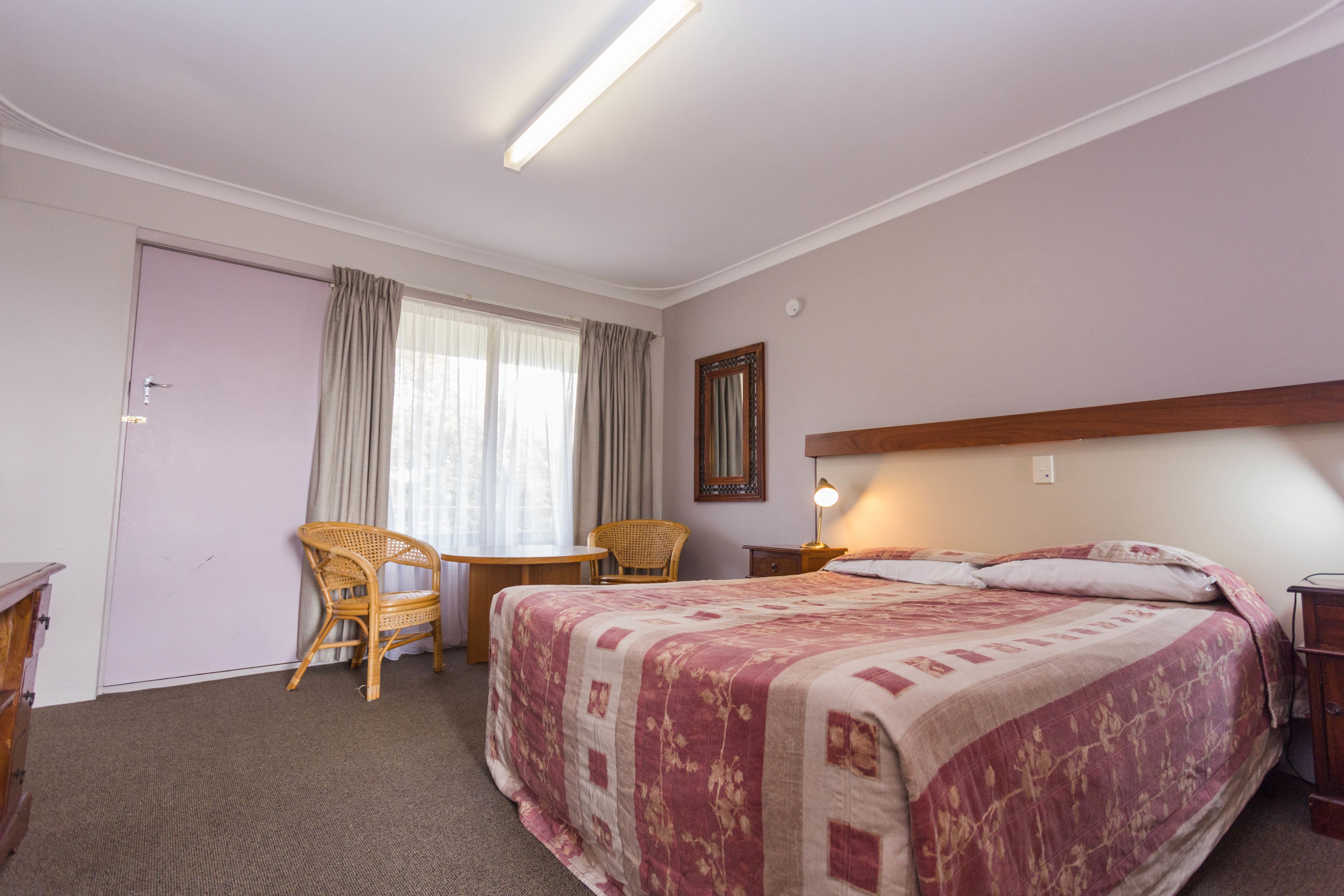 Une chambre d’hôtel avec un lit, une chaise, une petite table et un bureau.