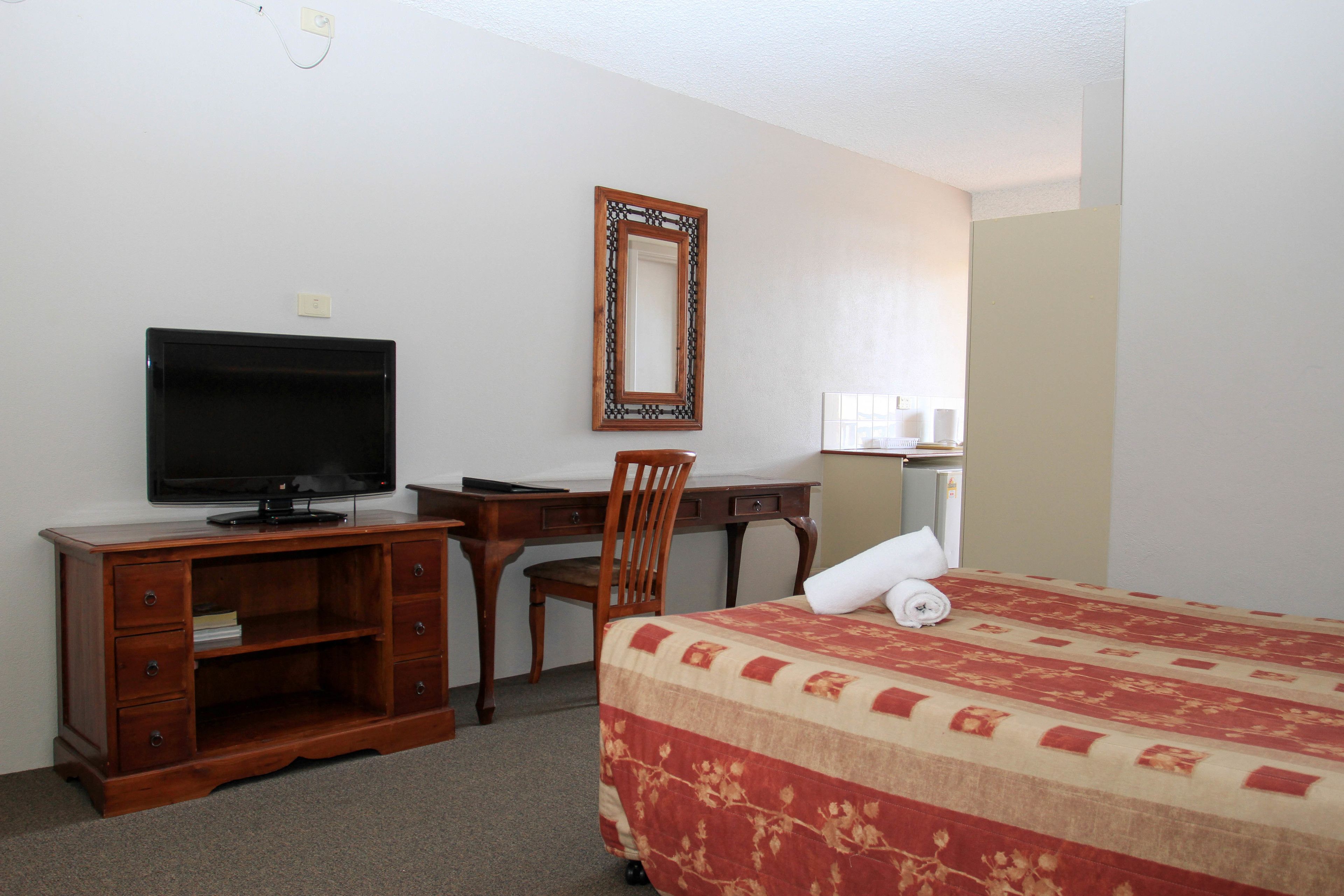 Ein Hotelzimmer mit einem Bett, einem Schreibtisch mit Fernseher, einem Stuhl und einem Spiegel.