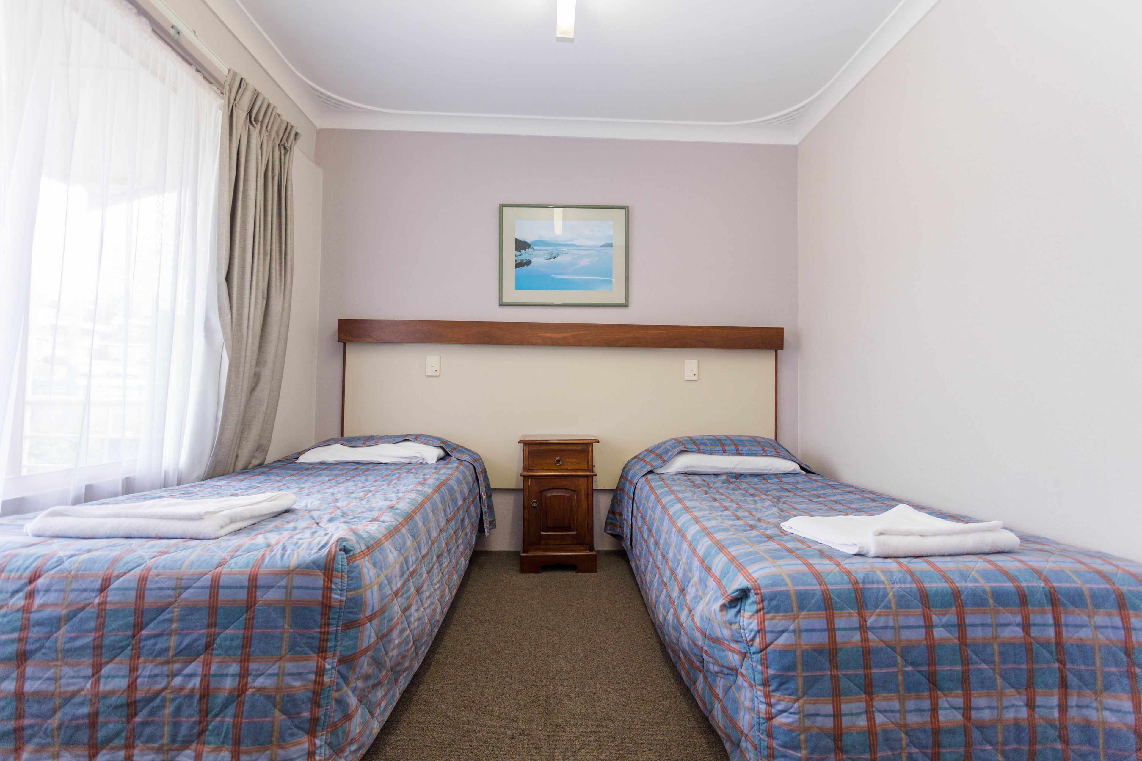 Una habitación con dos camas, una mesita de noche, un cuadro en la pared y un ventanal con cortinas.