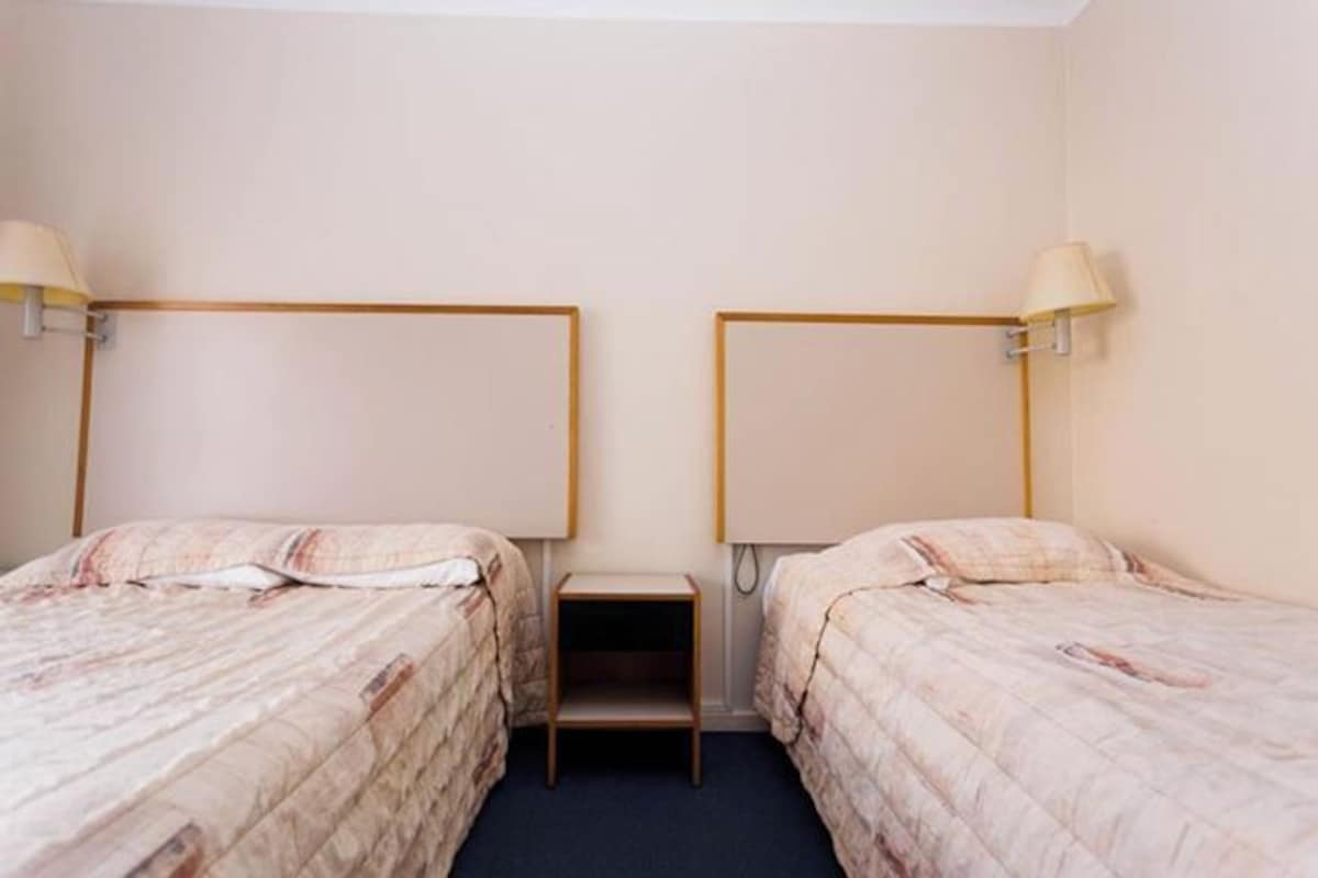 A hotel room with two single beds, each with a headboard, a small bedside table, and a lamp.