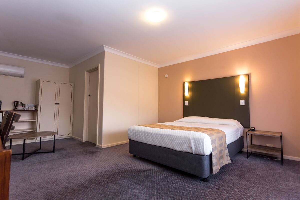 A hotel room with a bed, bedside table, and a desk with a chair.