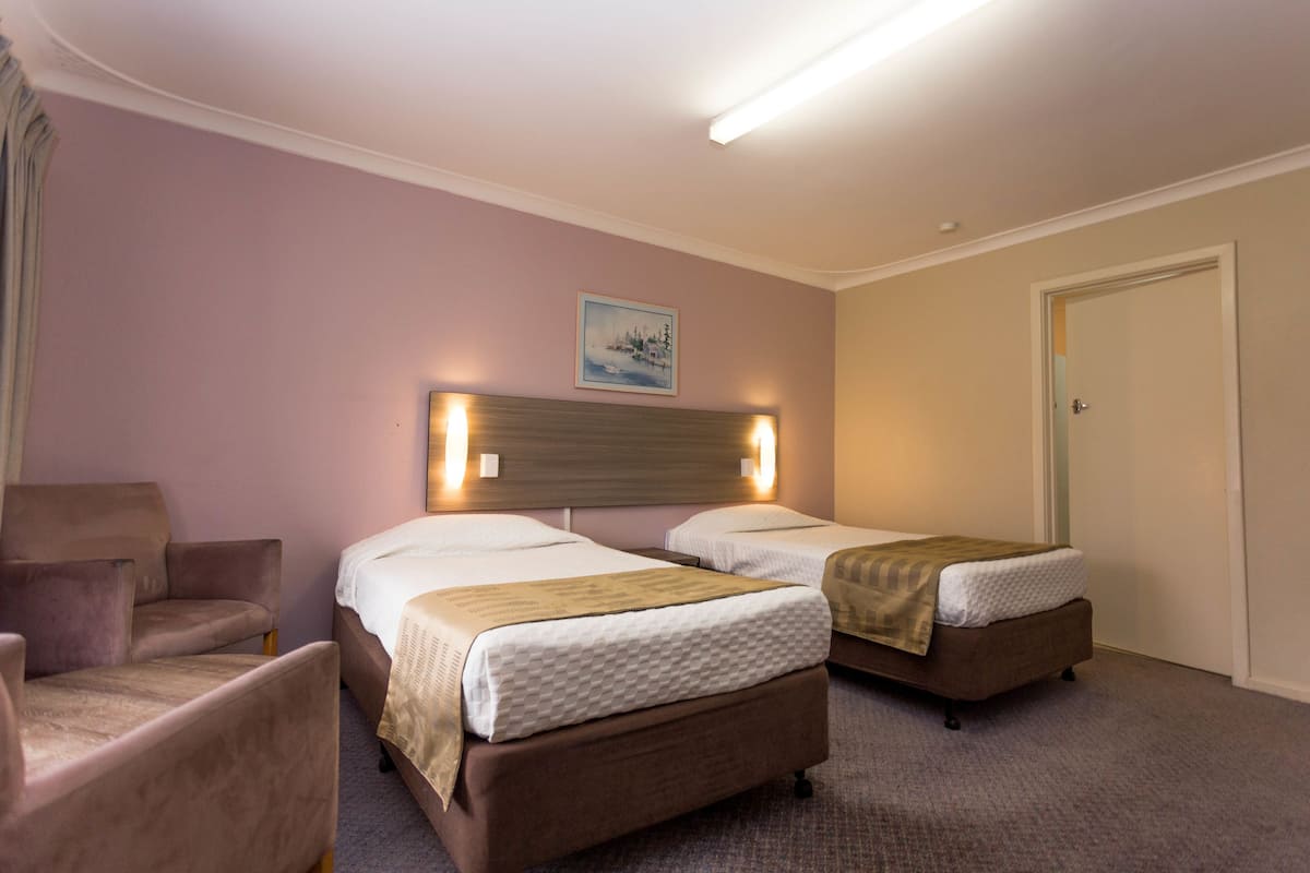 A hotel room with two beds, a chair, and a painting on the wall.