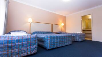 A hotel room with three beds, each with a blue plaid bedspread, a nightstand, and a wall-mounted lamp.