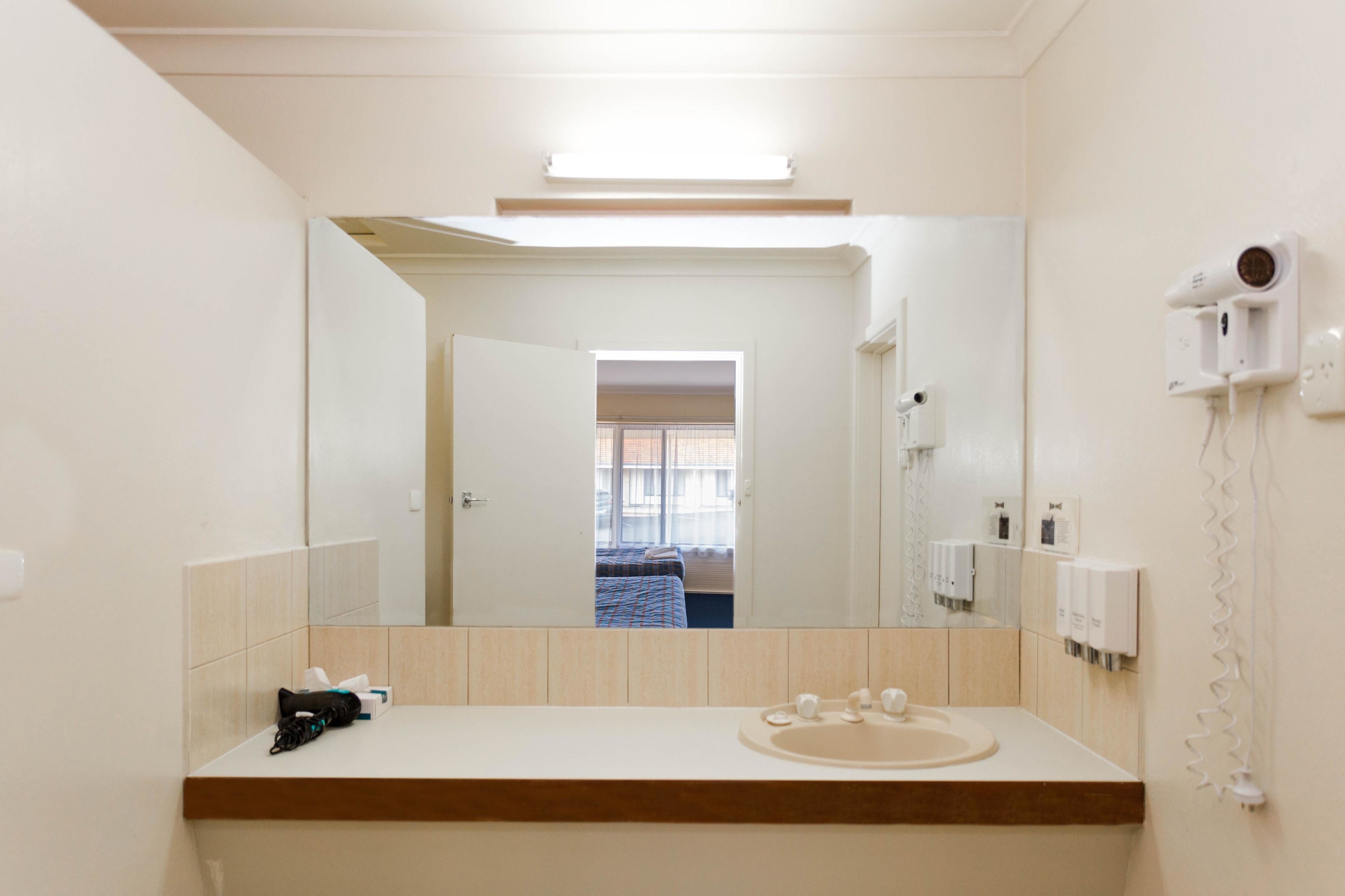 Un baño de hotel con un espejo grande, un lavamanos, un secador de pelo y una ventana con vistas a la habitación.
