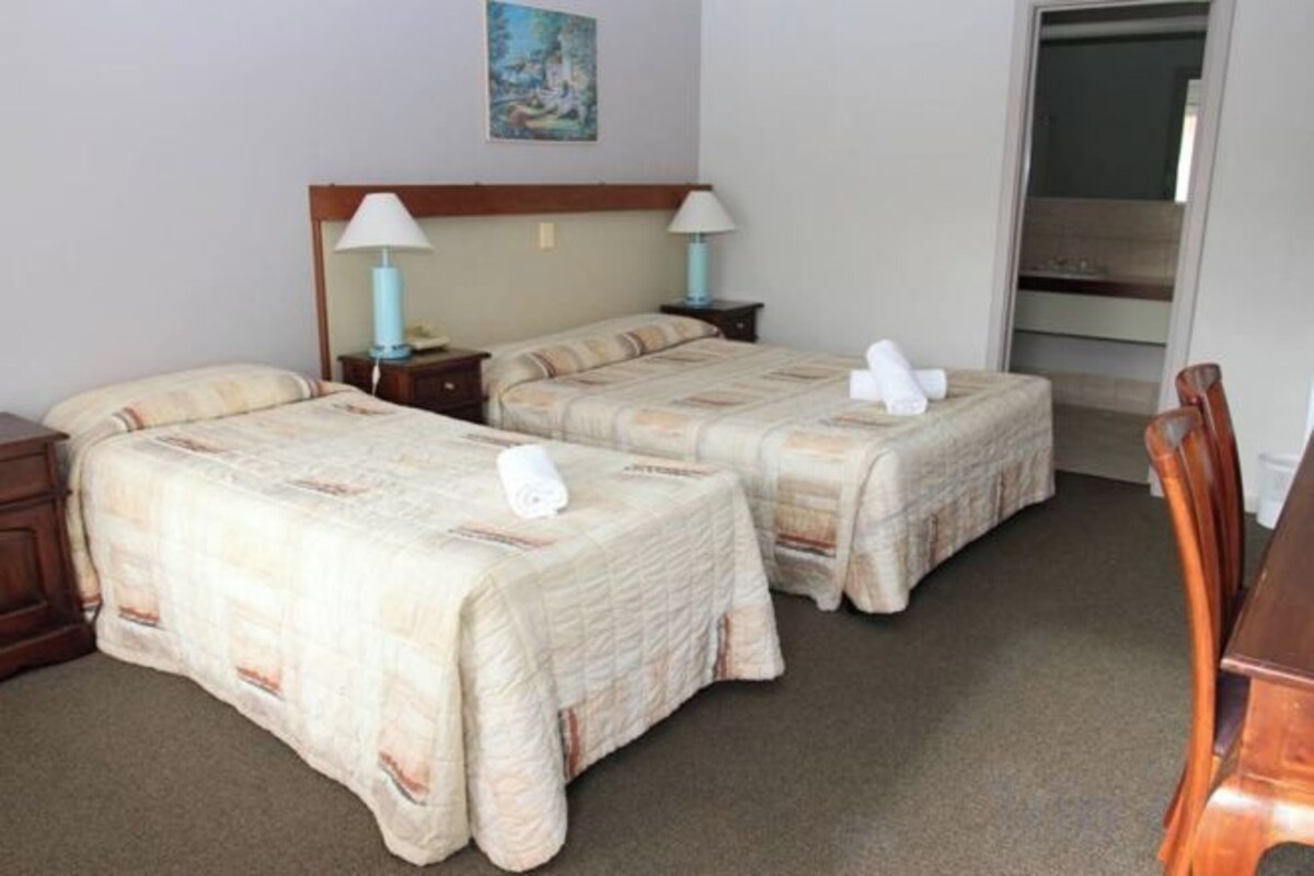 Habitación de hotel con dos camas, cabecero de madera, lámparas de noche, escritorio de madera y una silla.