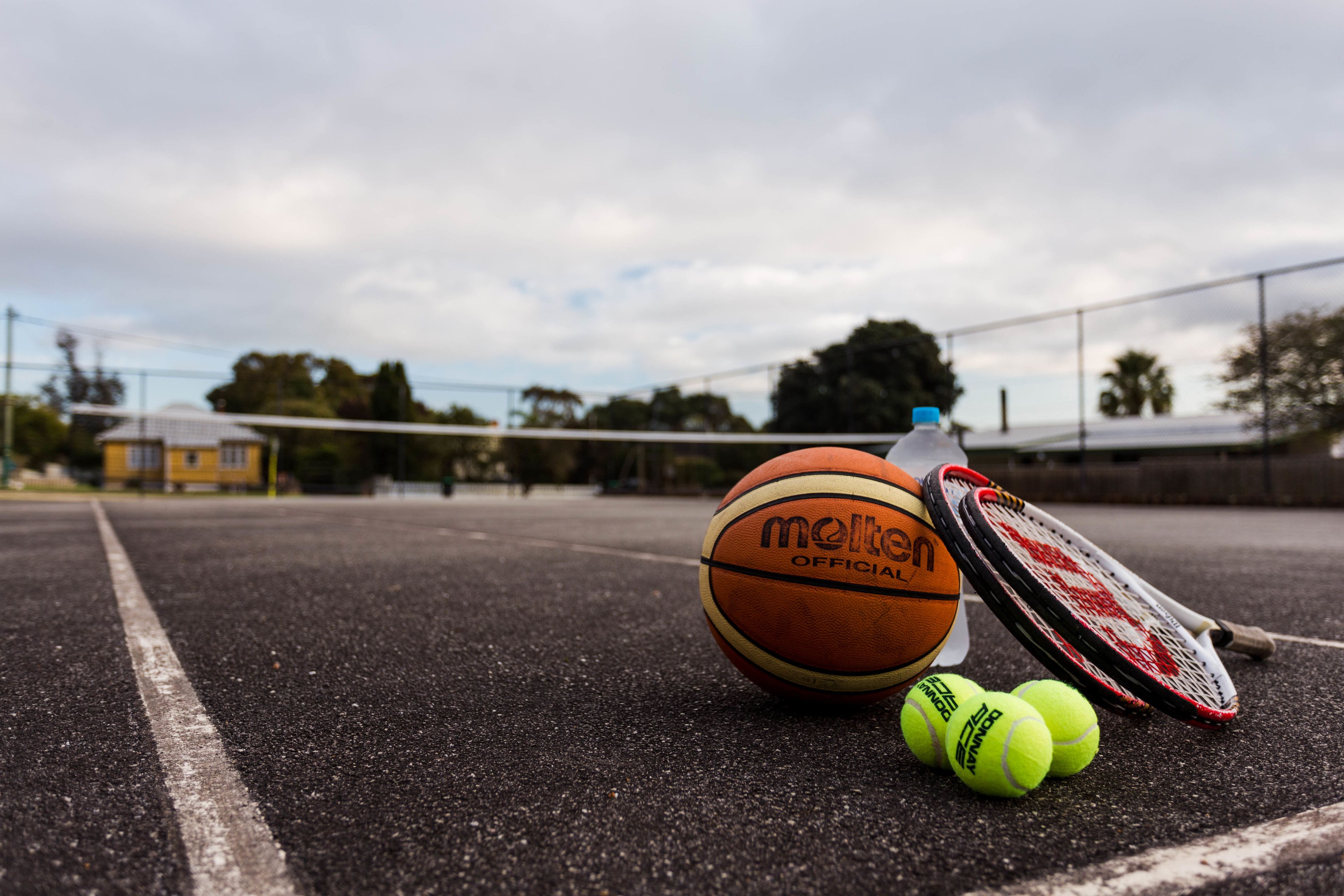 A sports court with a basketball, tennis racket, and tennis balls.