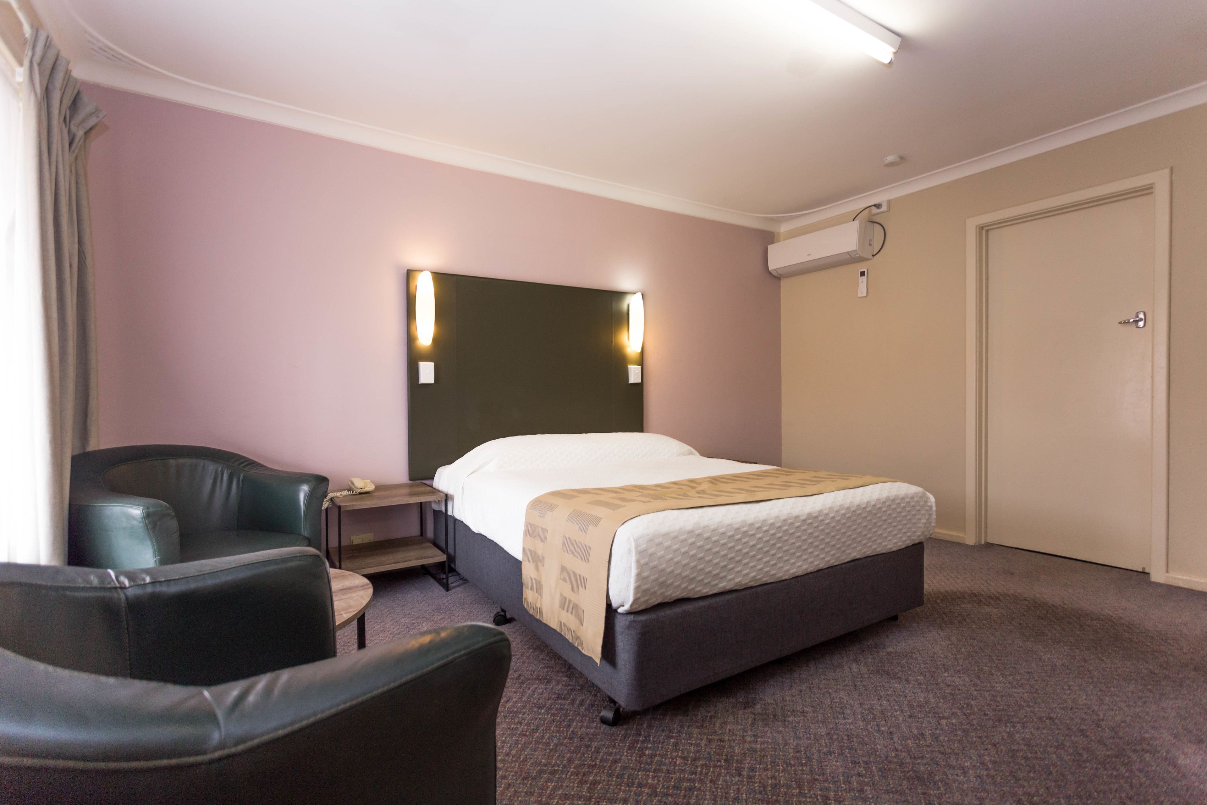A hotel room with a bed, a desk, a chair, and a wardrobe.