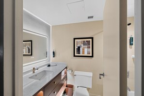 A bathroom with a sink, mirror, toilet, and a framed picture on the wall.