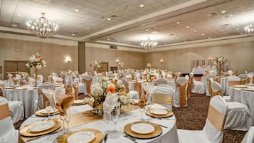 A banquet hall with round tables set for a formal event, featuring white tablecloths, gold chargers, and floral centerpieces.