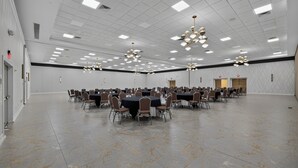 Une grande salle de conférence dotée de nombreuses tables et chaises, d’un plafond haut avec des luminaires encastrés et d’un sol en marbre.