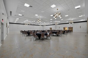 Une grande salle de conférence dotée de nombreuses tables et chaises, d’un plafond haut avec des luminaires encastrés et d’un sol en marbre.