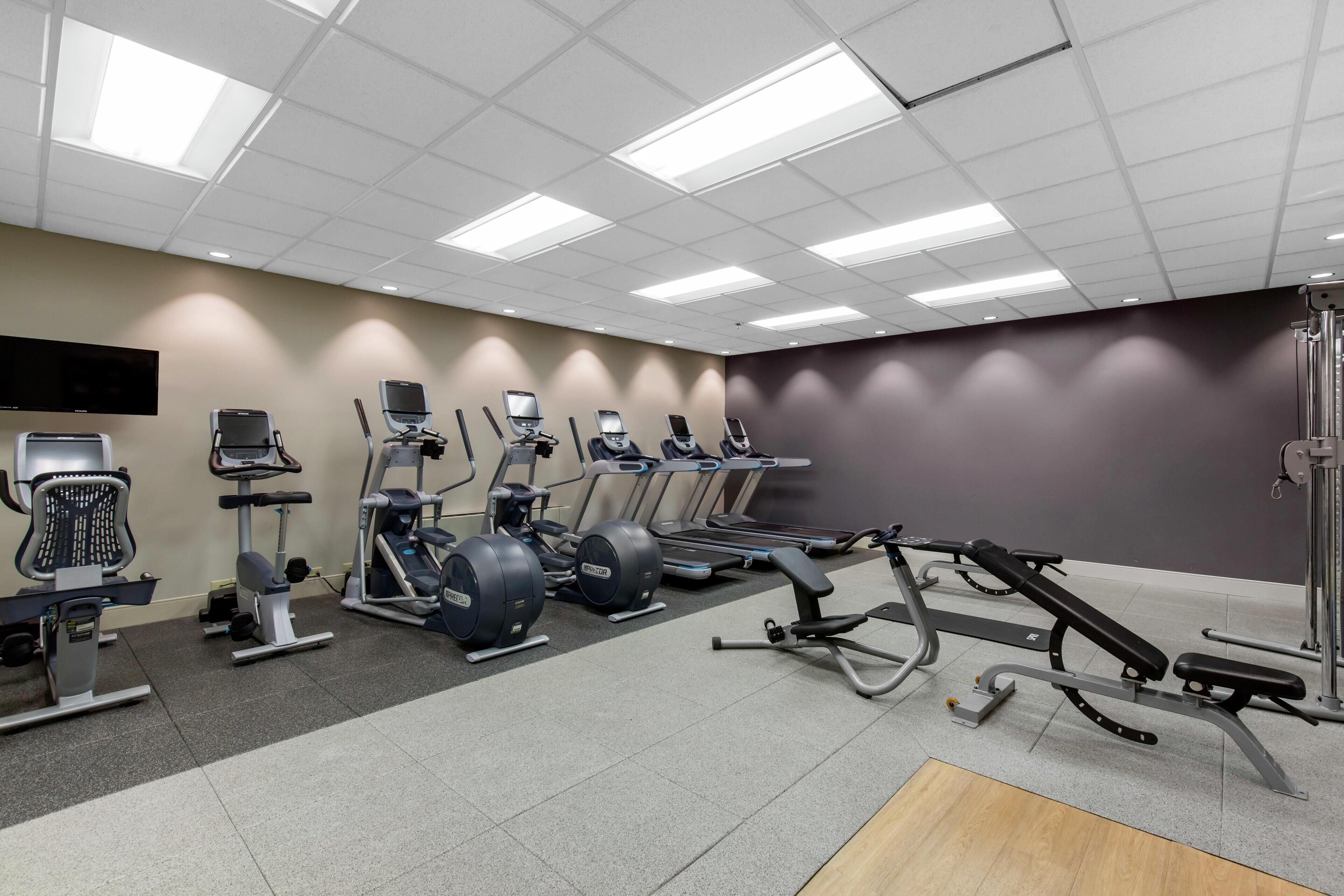 Une salle de sport équipée de divers appareils d’exercice, notamment des tapis de course, des appareils elliptiques et des bancs de musculation.