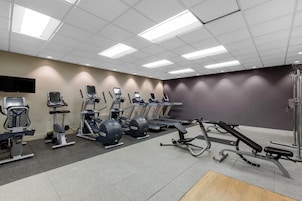 Un gimnasio con diversos equipos de ejercicio, incluyendo cintas de correr, elípticas y bancos de pesas.