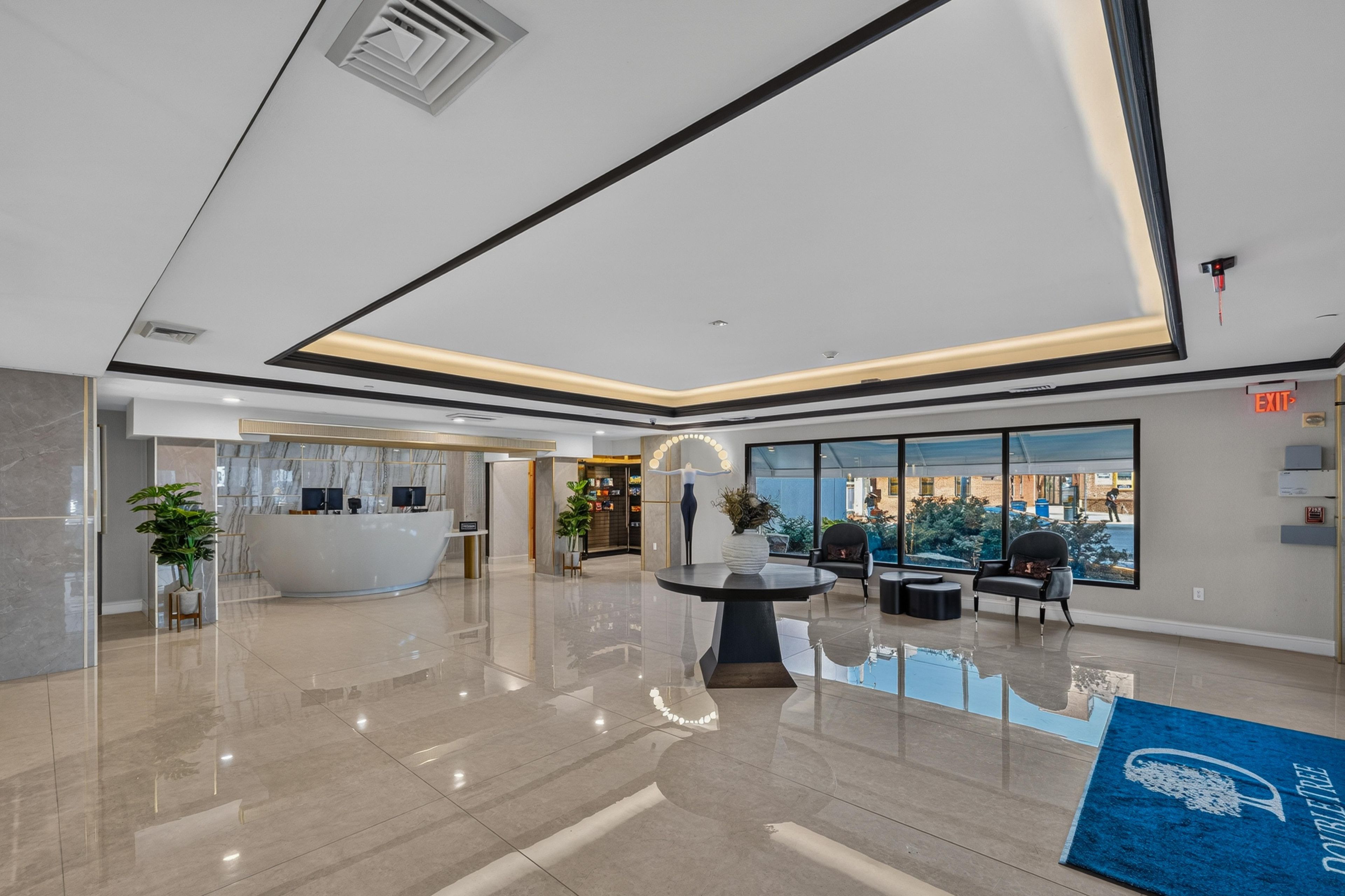 A modern lobby with a reception desk, seating area, and large windows offering a view of the outdoors.