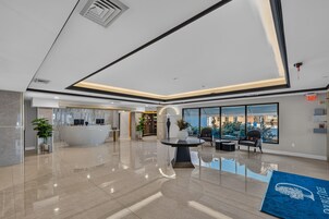 A modern lobby with a reception desk, seating area, and large windows offering a view of the outdoors.