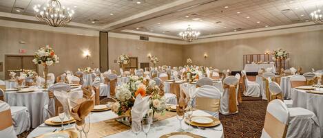 A banquet hall with round tables, white tablecloths, gold accents, and chandeliers.
