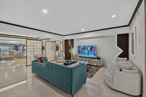 A modern living room with a teal sofa, white armchairs, a flat-screen TV, and a decorative partition.