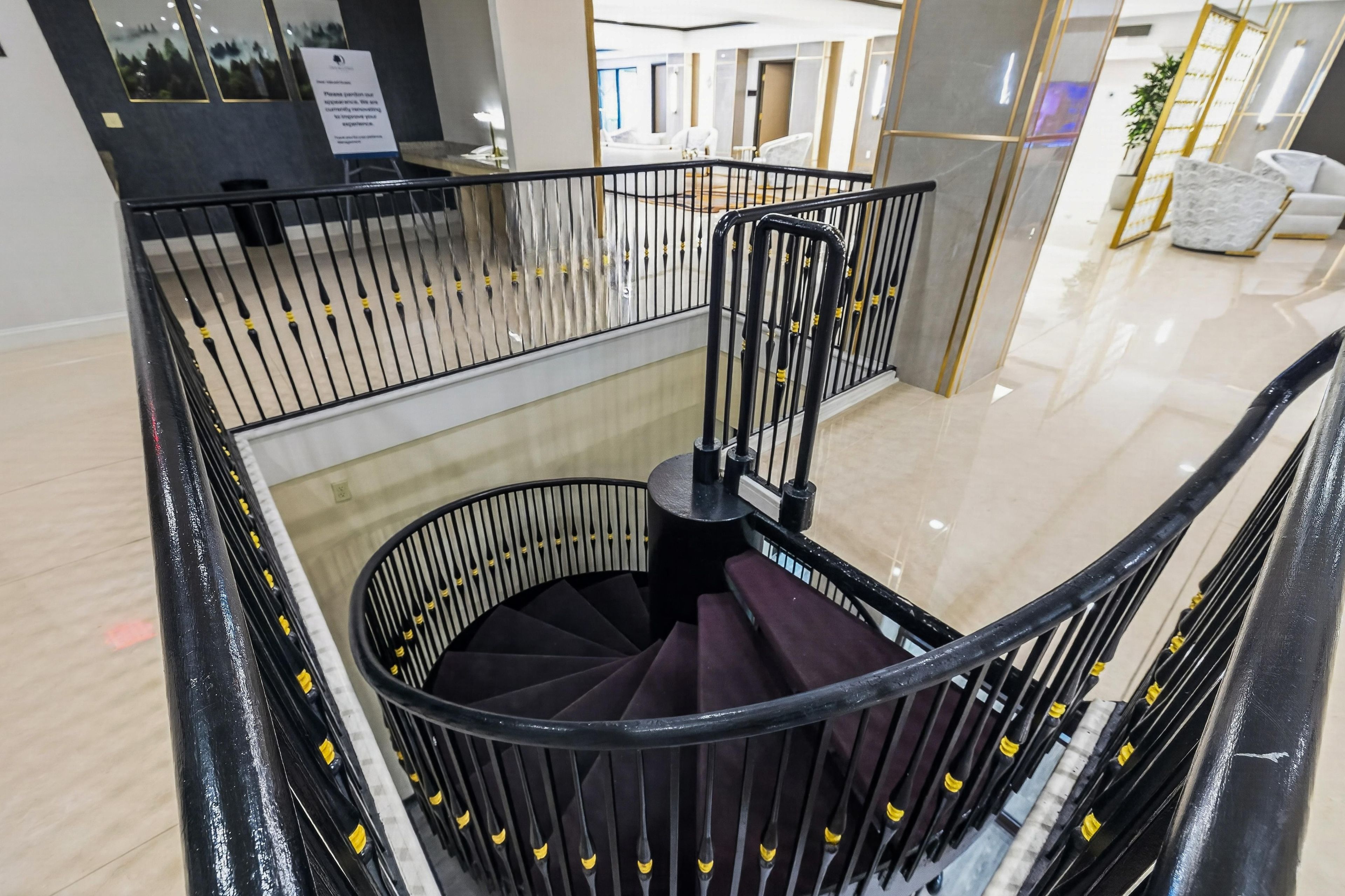 A modern interior with a black spiral staircase, a glass railing, and a view of a well-lit room with a white sofa.