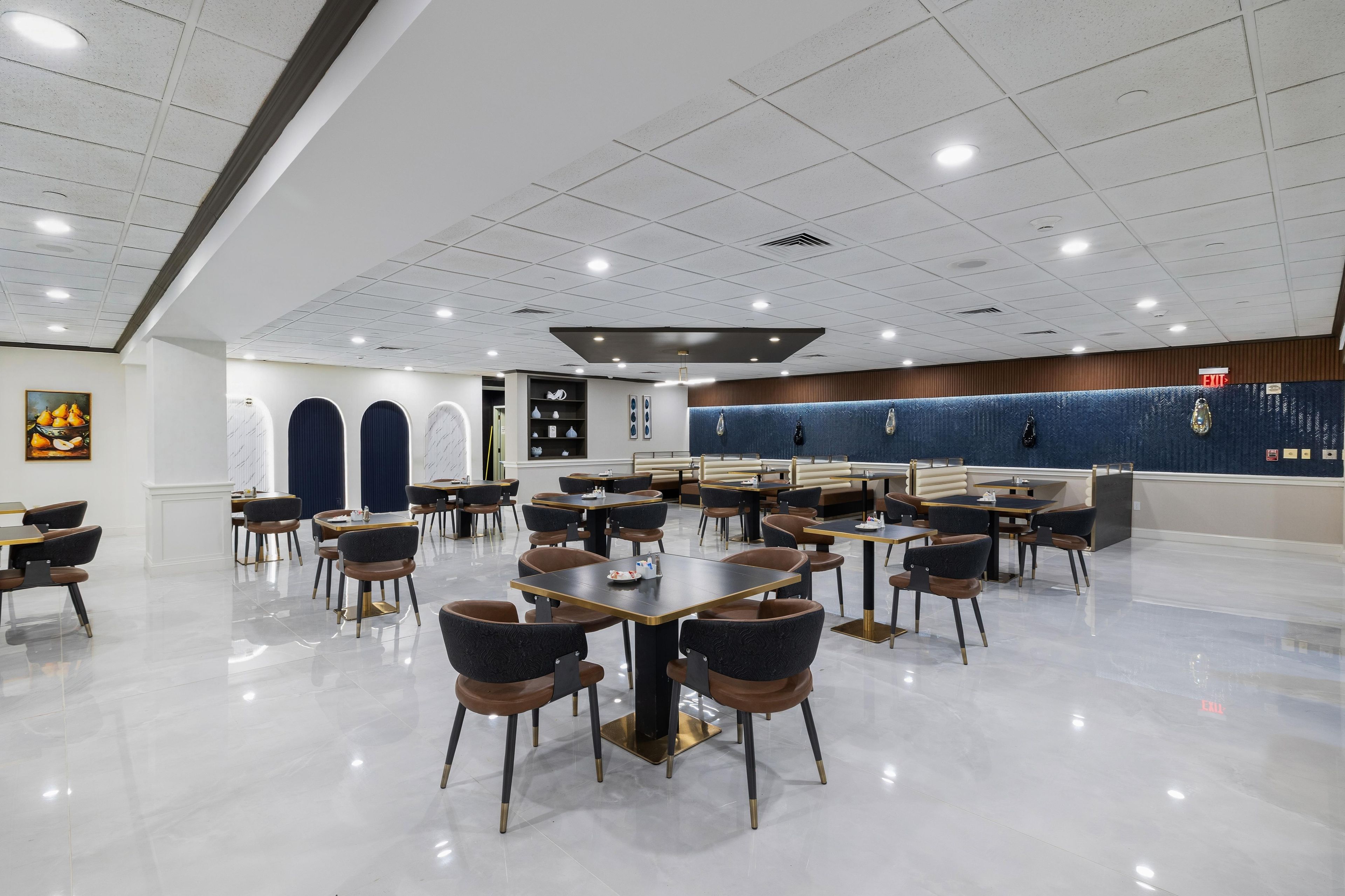 Un comedor amplio con varias mesas y sillas, una pared de acento azul, e iluminación empotrada en el techo.