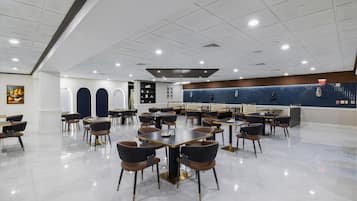 Un comedor amplio con varias mesas y sillas, una pared de acento azul, e iluminación empotrada en el techo.