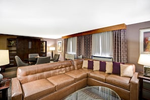 A modern living room with a leather sectional sofa, a dining area with a table and chairs, and a large window with patterned curtains. - DoubleTree by Hilton Downtown Wilmington - Legal District (Wilmington)