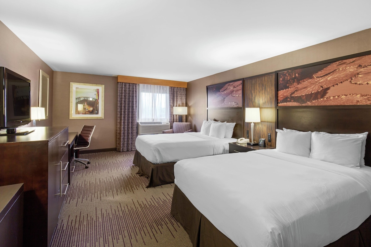 A hotel room with two beds, a desk, a television, and a large painting on the wall.