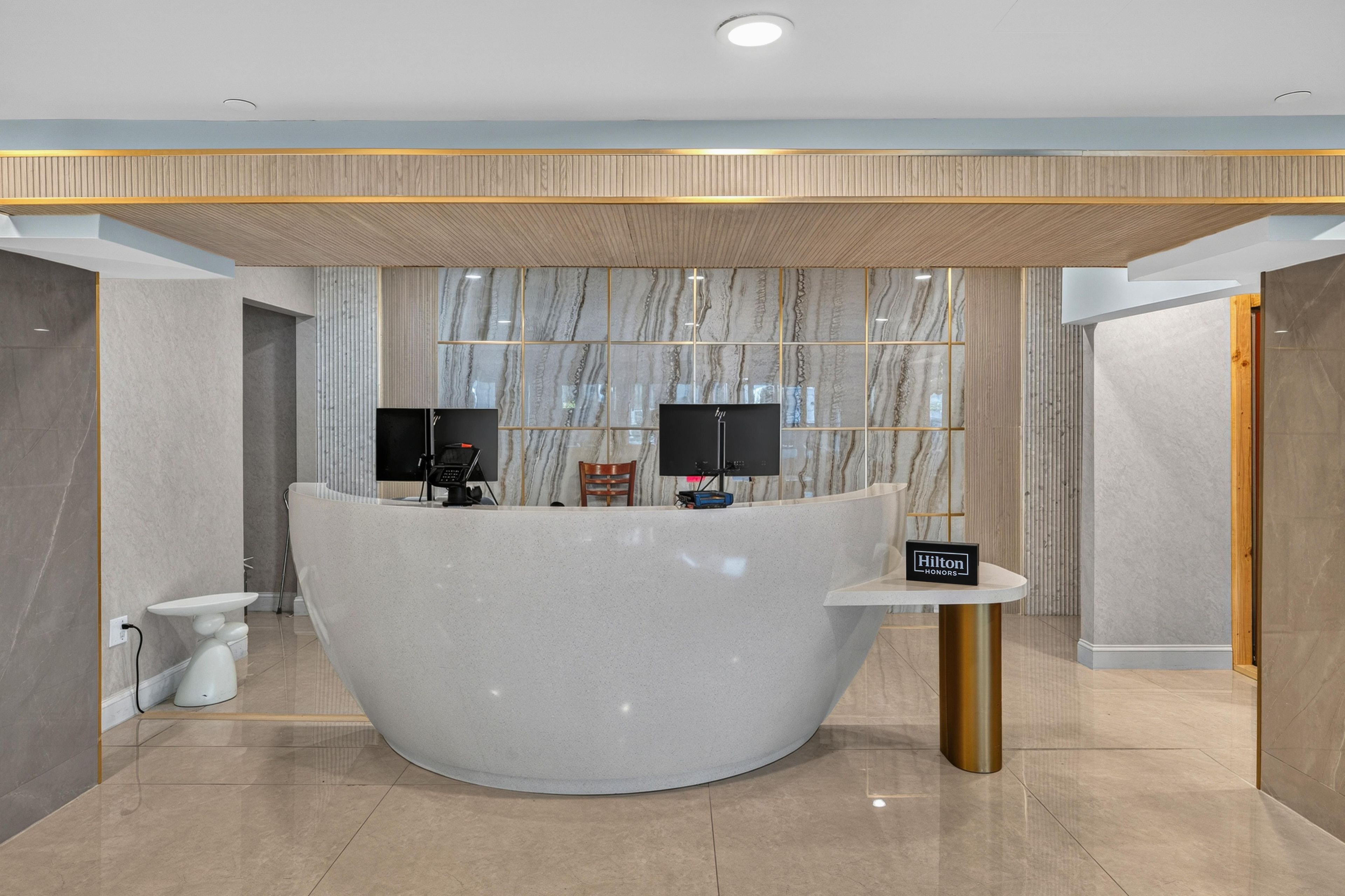 A modern reception desk with a marble backdrop, a flat-screen TV, and a 'Hilton Honors' sign.