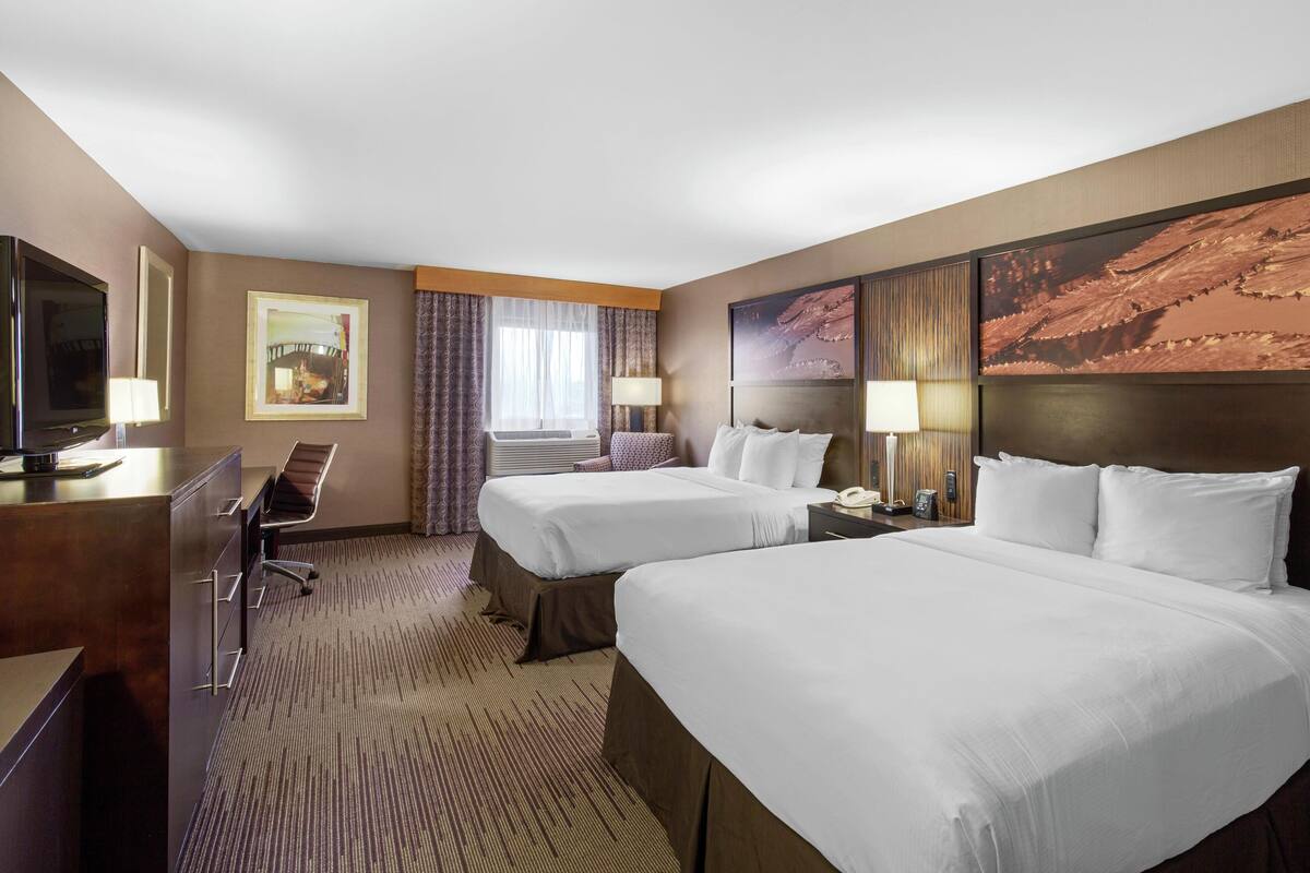 A hotel room with two beds, a desk, a television, and a large painting on the wall.
