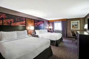Una habitación de hotel con dos camas, un escritorio, una silla, una lámpara y un cuadro en la pared.