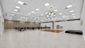 Una amplia sala de conferencias con un piso de baile central, varias mesas con sillas y un moderno candelabro.