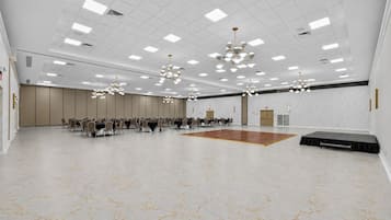 A spacious conference room with a central dance floor, multiple tables with chairs, and a modern chandelier.