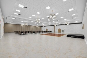 A spacious conference room with a central dance floor, multiple tables with chairs, and a modern chandelier.