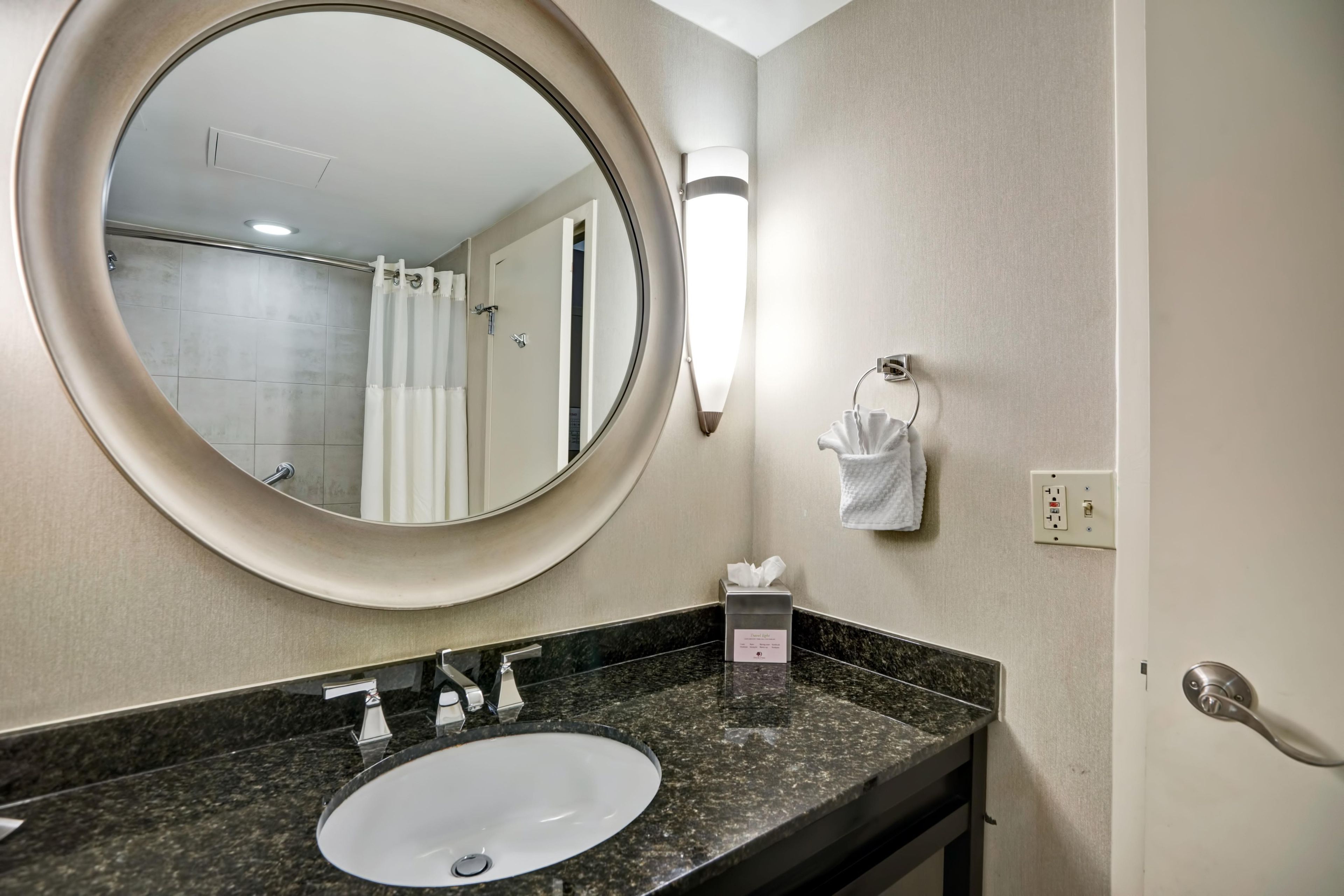 A bathroom with a round mirror, a sink, a towel rack, and a shower curtain.