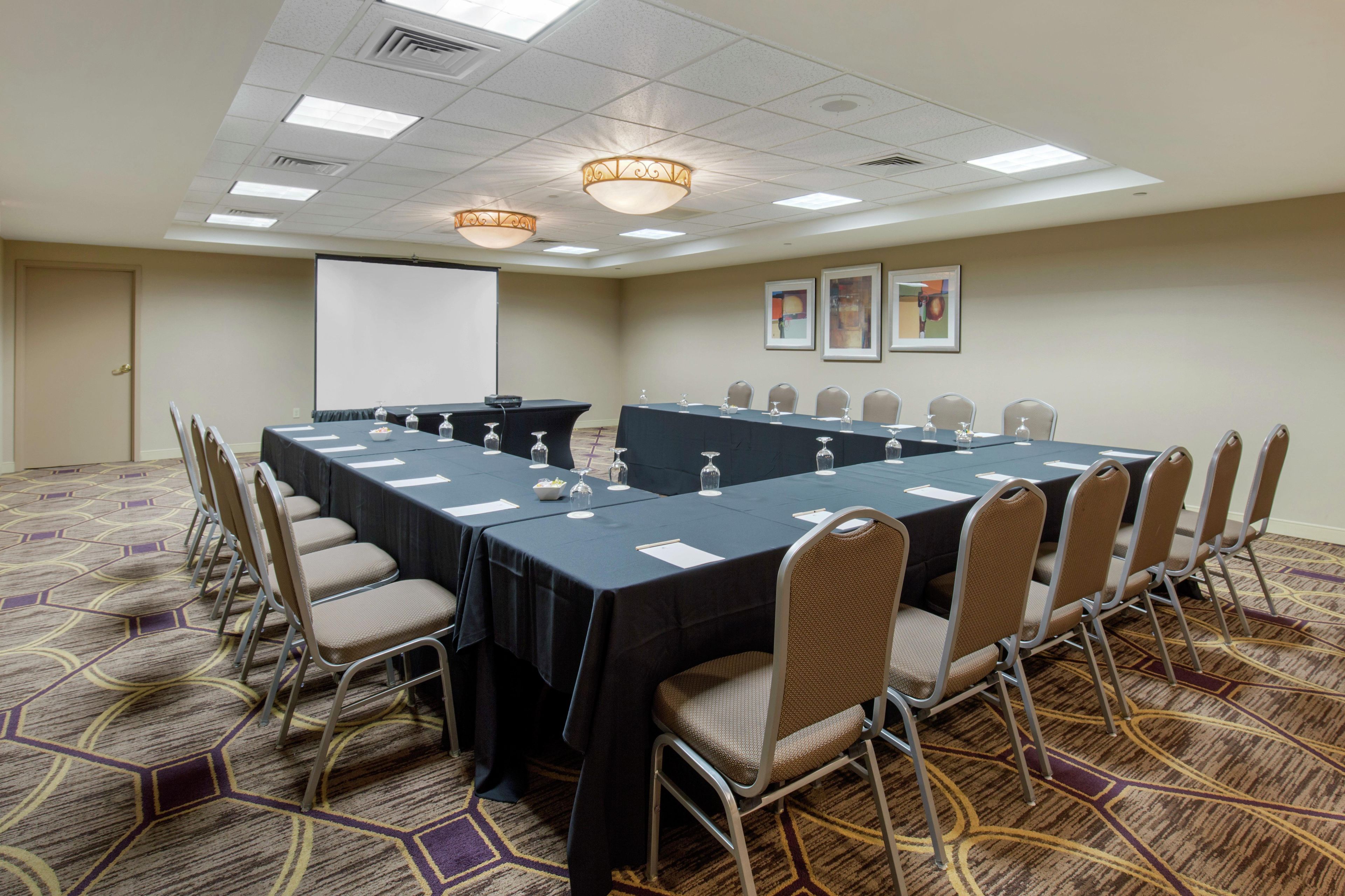 A conference room with a long table, chairs, a projector screen, and framed pictures on the wall.