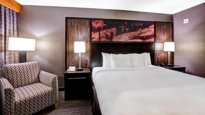 Habitación de hotel con una cama grande, dos mesitas de noche, una silla y un televisor montado en la pared.