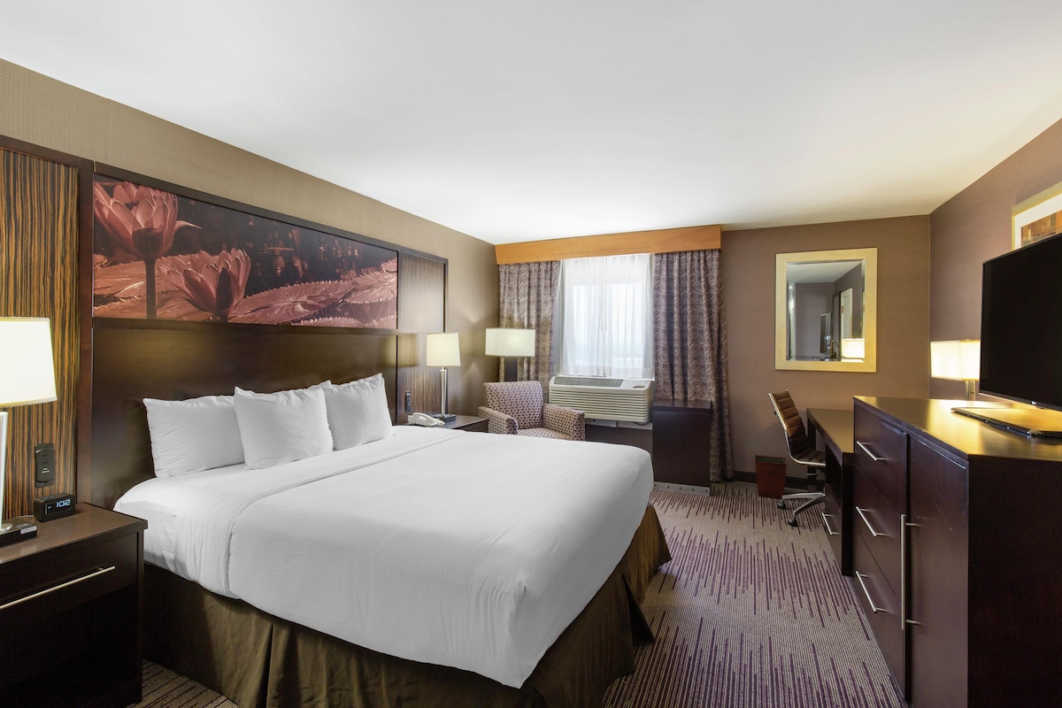 A hotel room with a large bed, a desk with a chair, a TV, and a window with curtains.