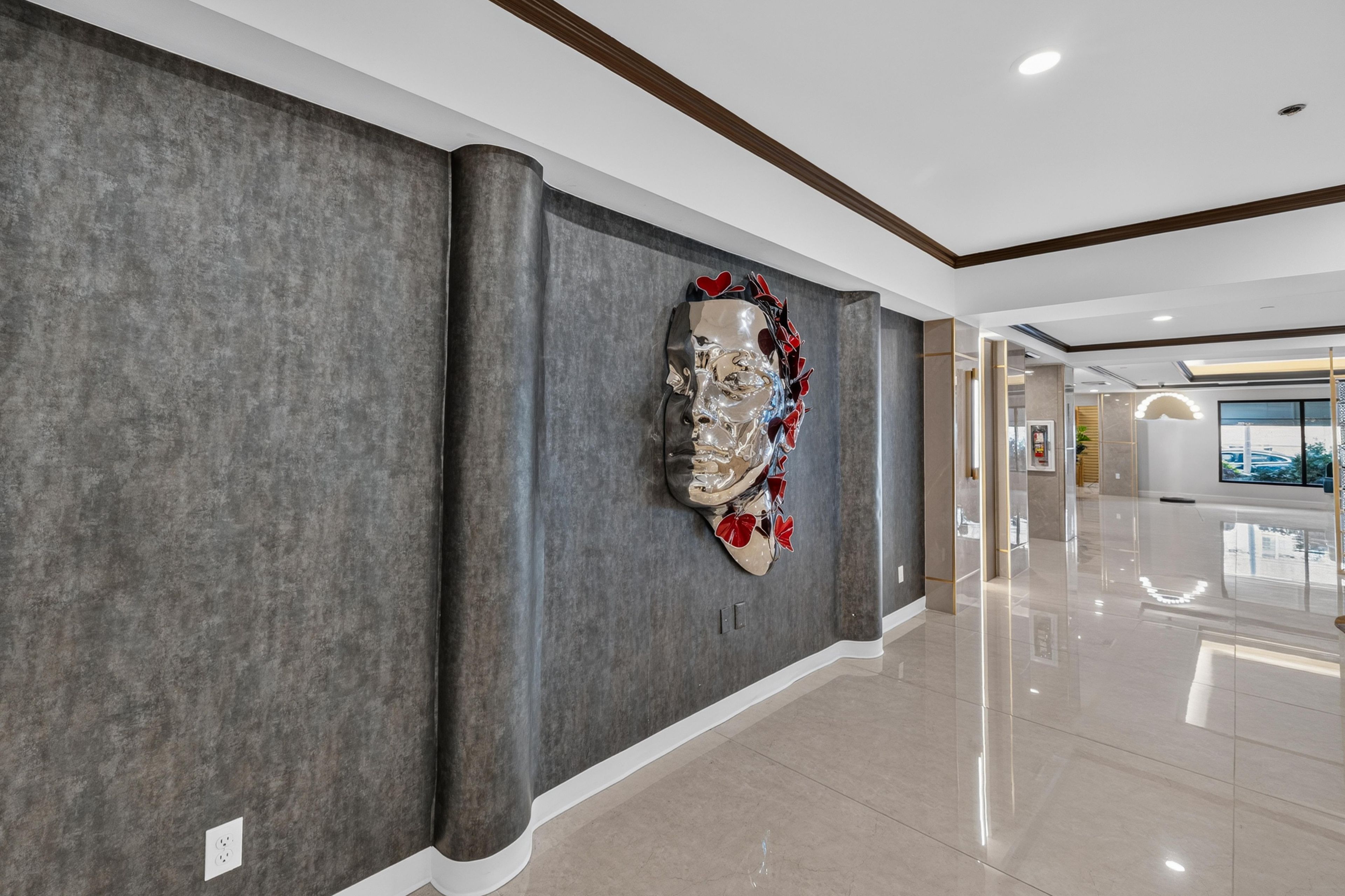 A hallway with a modern art sculpture on the wall, a polished floor, and a view of the outside through a window.