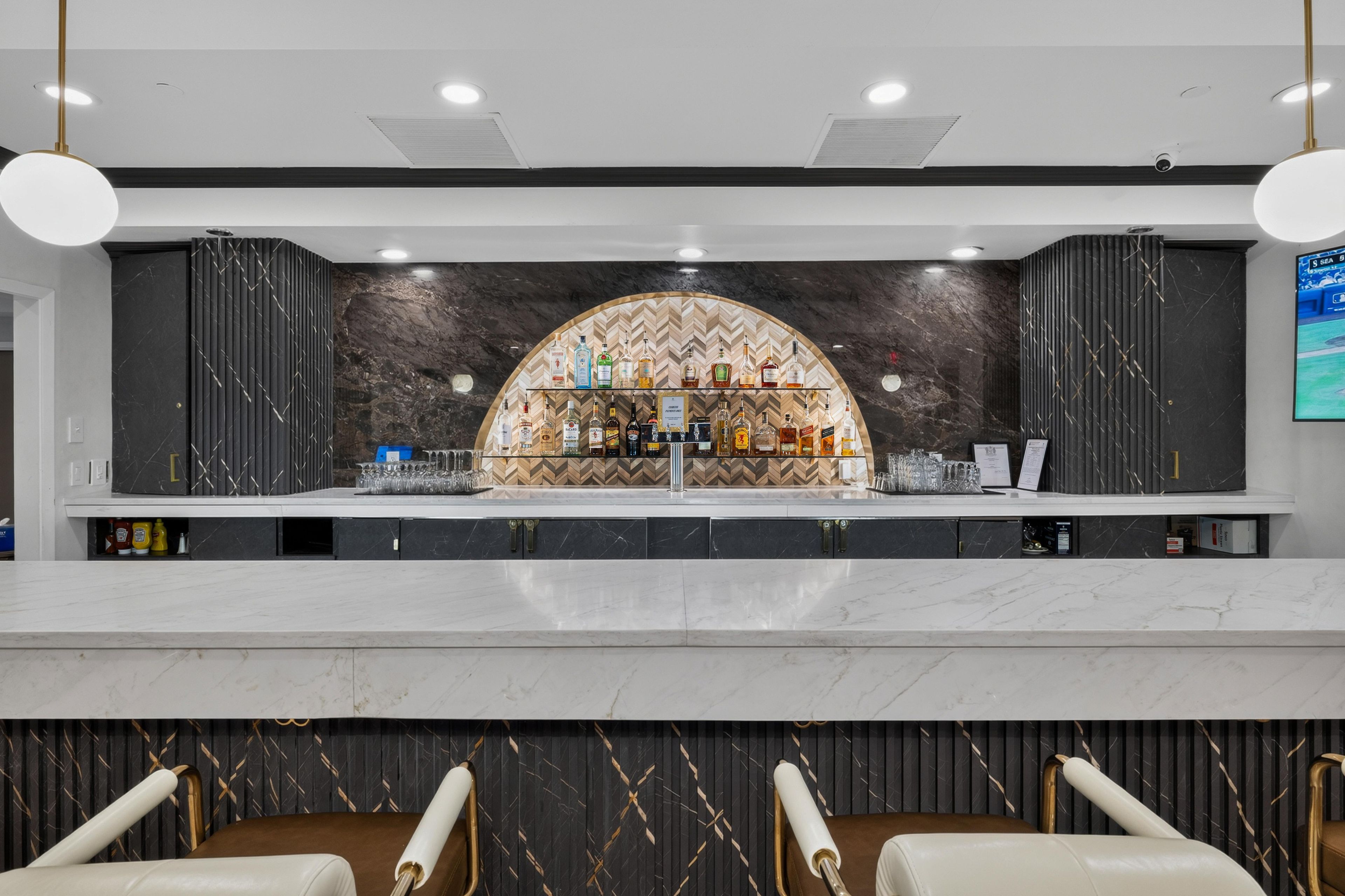 A bar area with a marble countertop, a selection of liquor bottles, and a herringbone patterned wall.