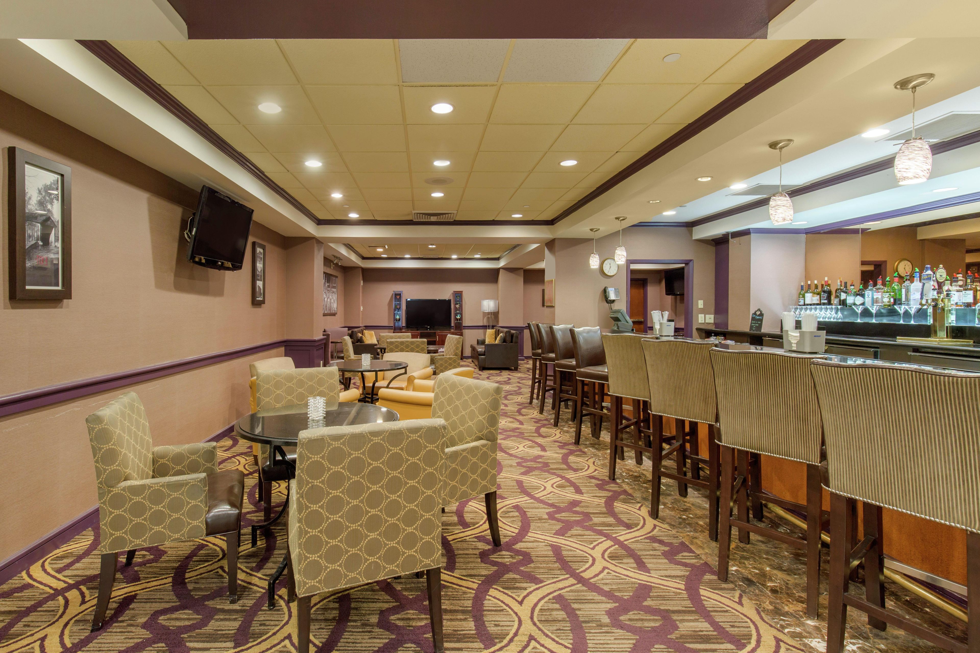 Un hall d’hôtel comprenant un bar, des espaces aménagés avec des sièges et un téléviseur fixé au mur.