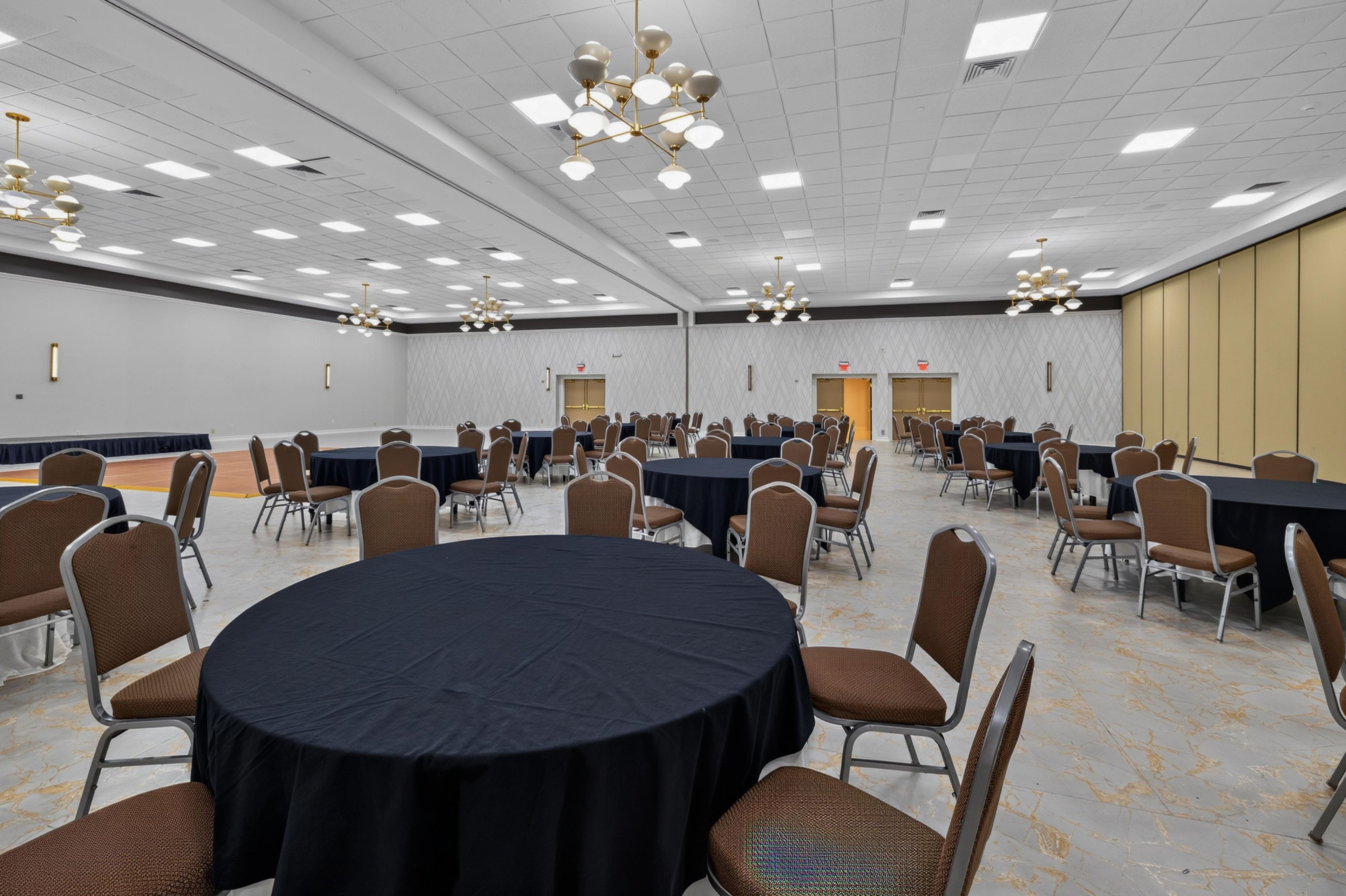 Een ruime congreszaal met meerdere tafels en stoelen, opgesteld in rijen.