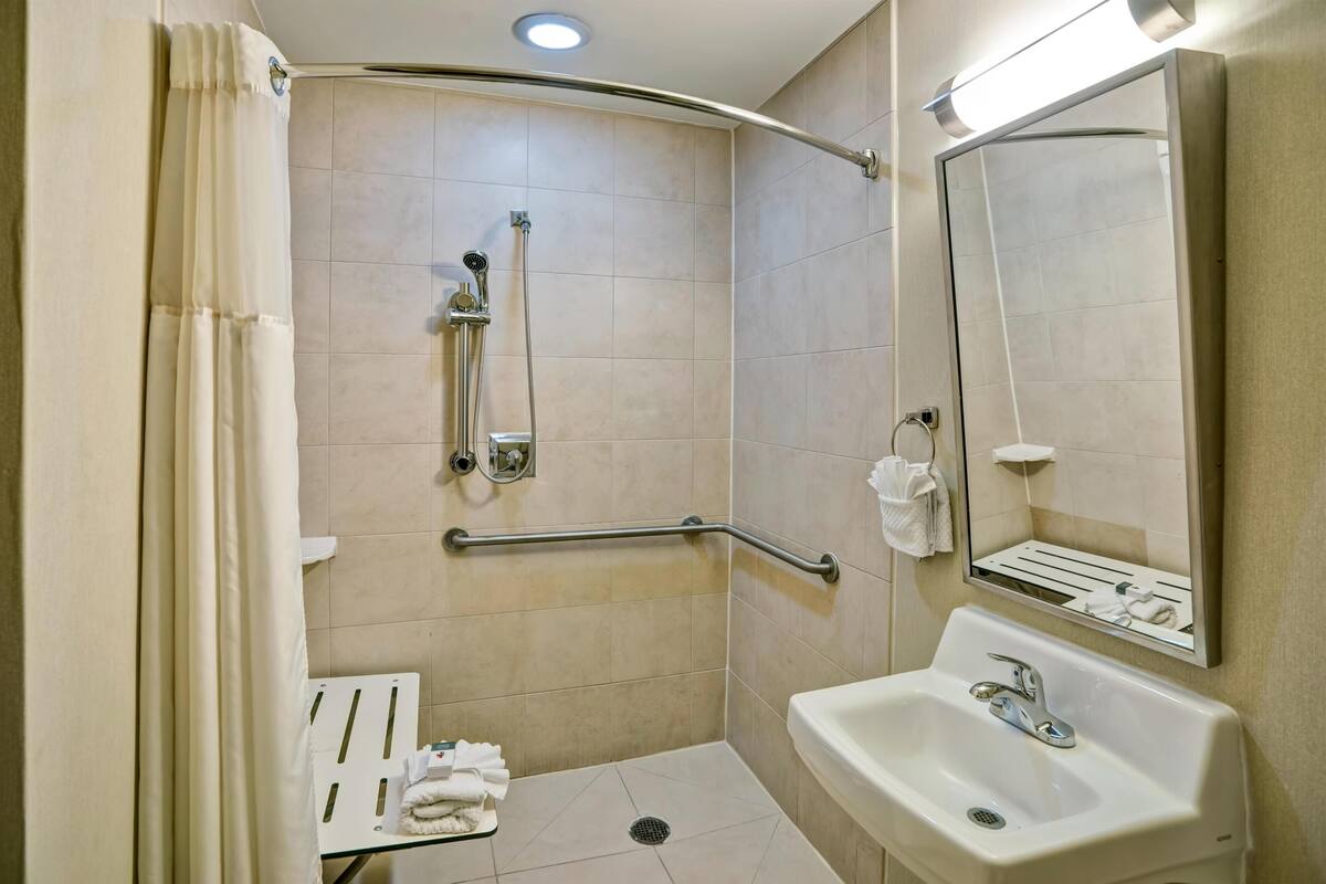 A handicap-accessible bathroom with a shower, grab bars, a sink, and a mirror.