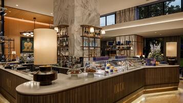 Un espace bar moderne avec un sol en marbre, des étagères en bois remplies de bouteilles et une vitrine où sont exposées des pâtisseries.