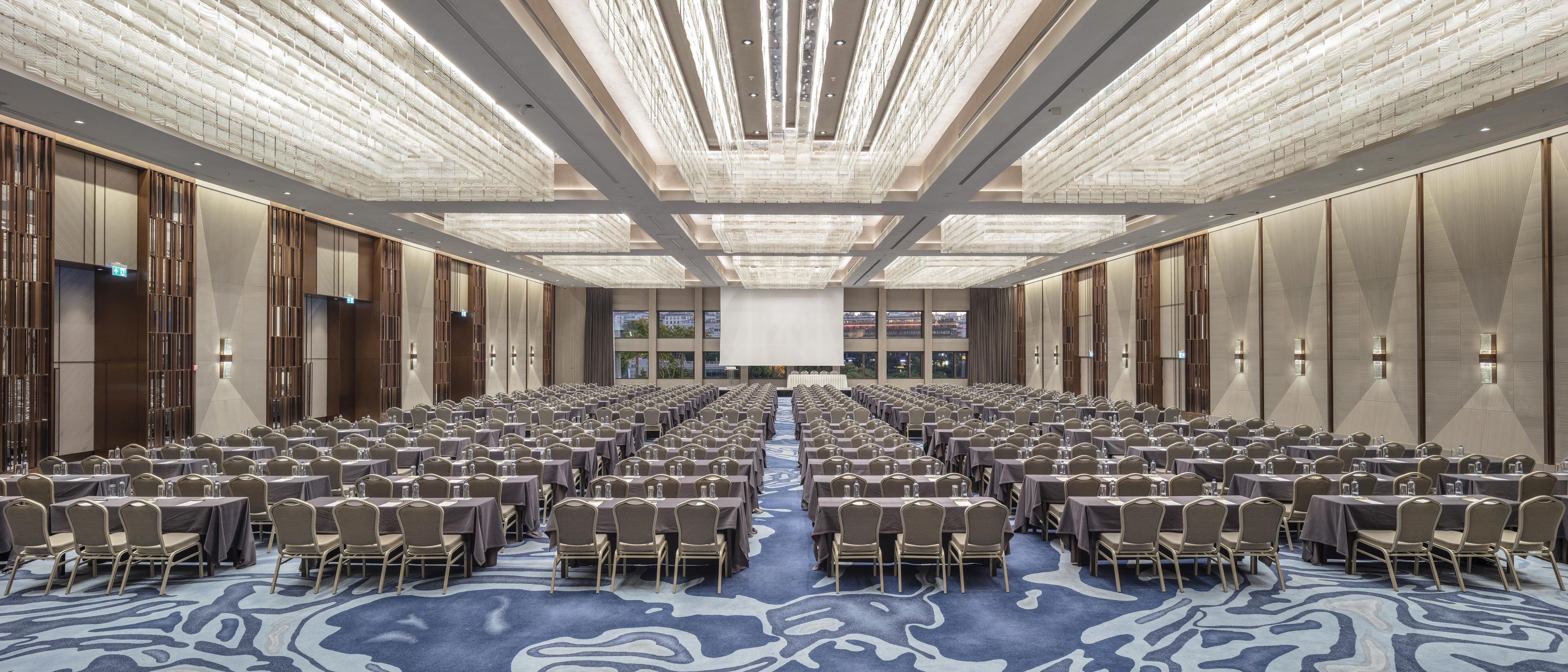 A large conference room with rows of tables and chairs, a central stage, and a patterned carpet.