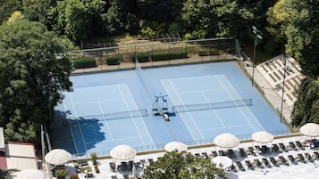 Una cancha de tenis exterior con asientos y sombrillas.