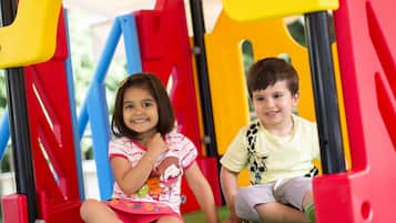 Two children sitting on a colorful play structure with a blue canopy.