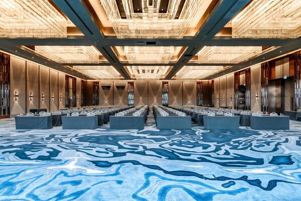 Une salle de conférence avec des rangées de tables et de chaises, une moquette à motifs et un design de plafond moderne.