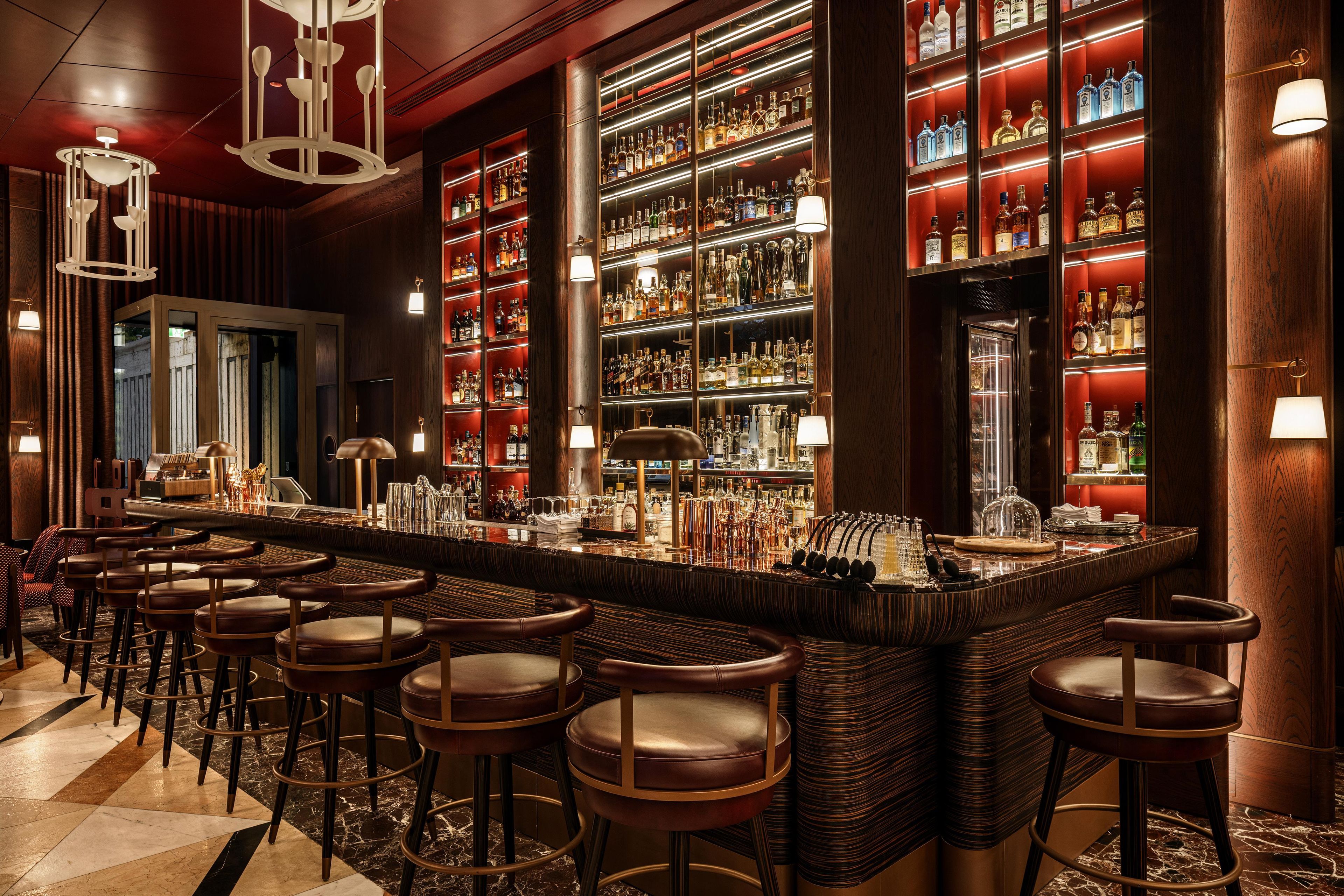 A bar area with multiple stools, a bar counter, and shelves stocked with bottles.